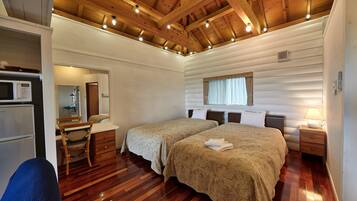 Una habitación acogedora de estilo cabaña con dos camas, techo de madera, kitchenette pequeña y una ventana con cortinas.