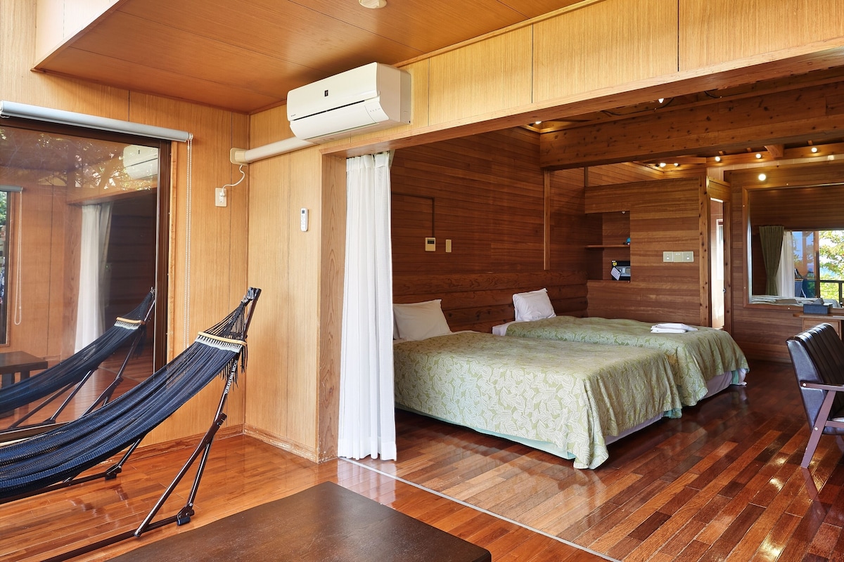 Een houten blokhut met een hangmat, twee bedden en een airconditioning.