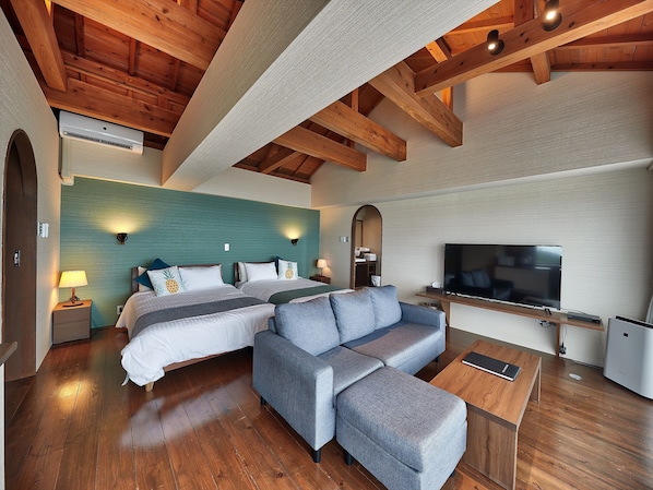 A modern hotel room with two beds, a grey sofa, a flat-screen TV, wooden flooring, and a wooden ceiling structure. - Nagahama Beach Resort Kanon (Nakijin)