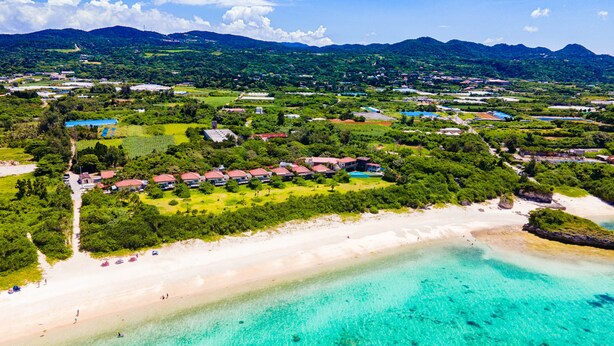 An aerial view of a coastal resort with beachfront properties, clear turquoise waters, and lush greenery. - Nagahama Beach Resort Kanon (Nakijin)