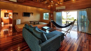 A wooden cabin interior with a sofa, hammock, and a TV mounted on the wall. - Nagahama Beach Resort Kanon (Nakijin)