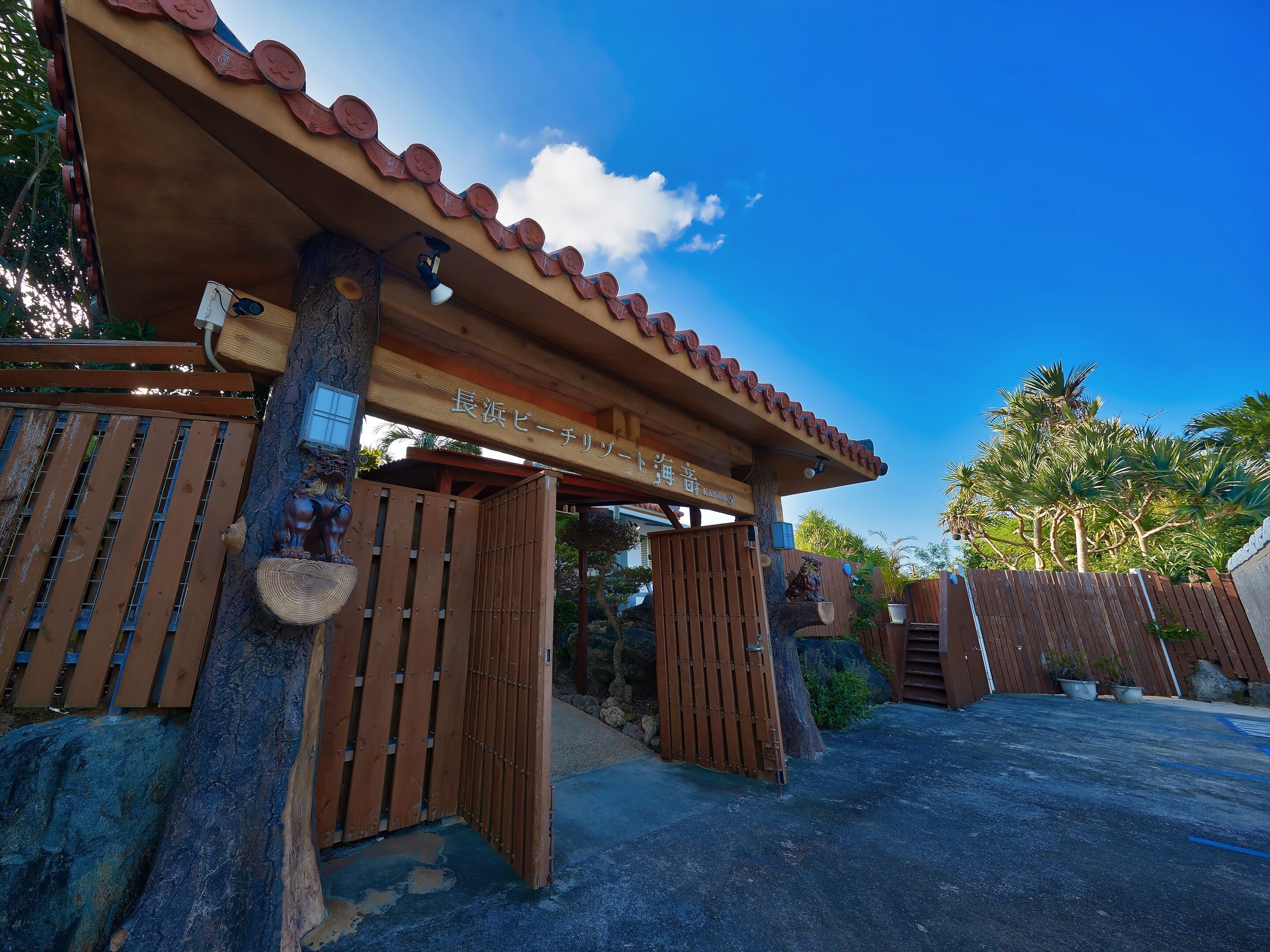 A wooden entrance gate with a sign above it, a tree trunk, and a clear blue sky.
