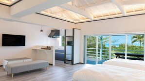 A modern bedroom with a large bed, a bench, a TV, and a kitchenette. - Nagahama Beach Resort Kanon (Nakijin)