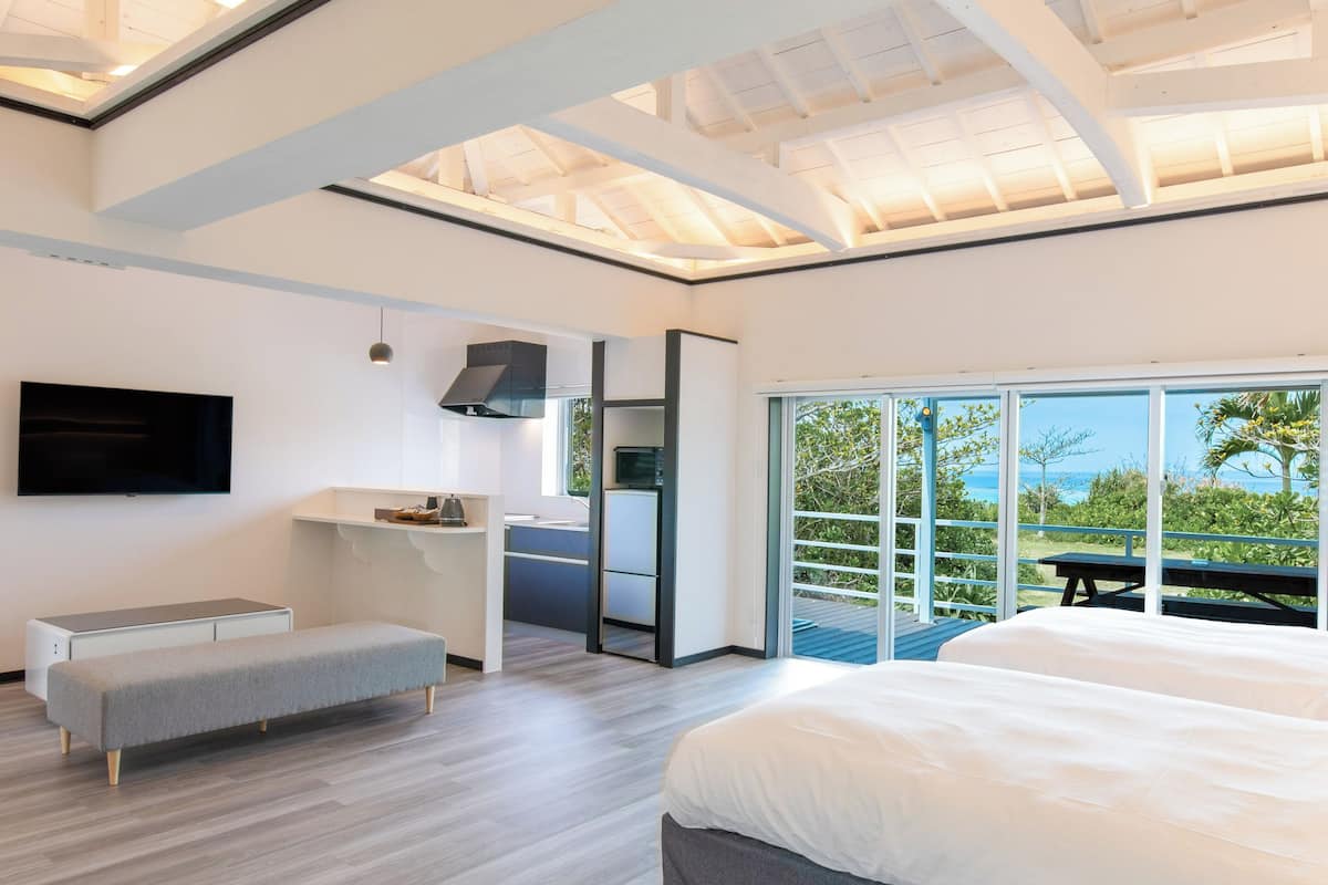 A modern bedroom with a large bed, a bench, a TV, and a kitchenette.