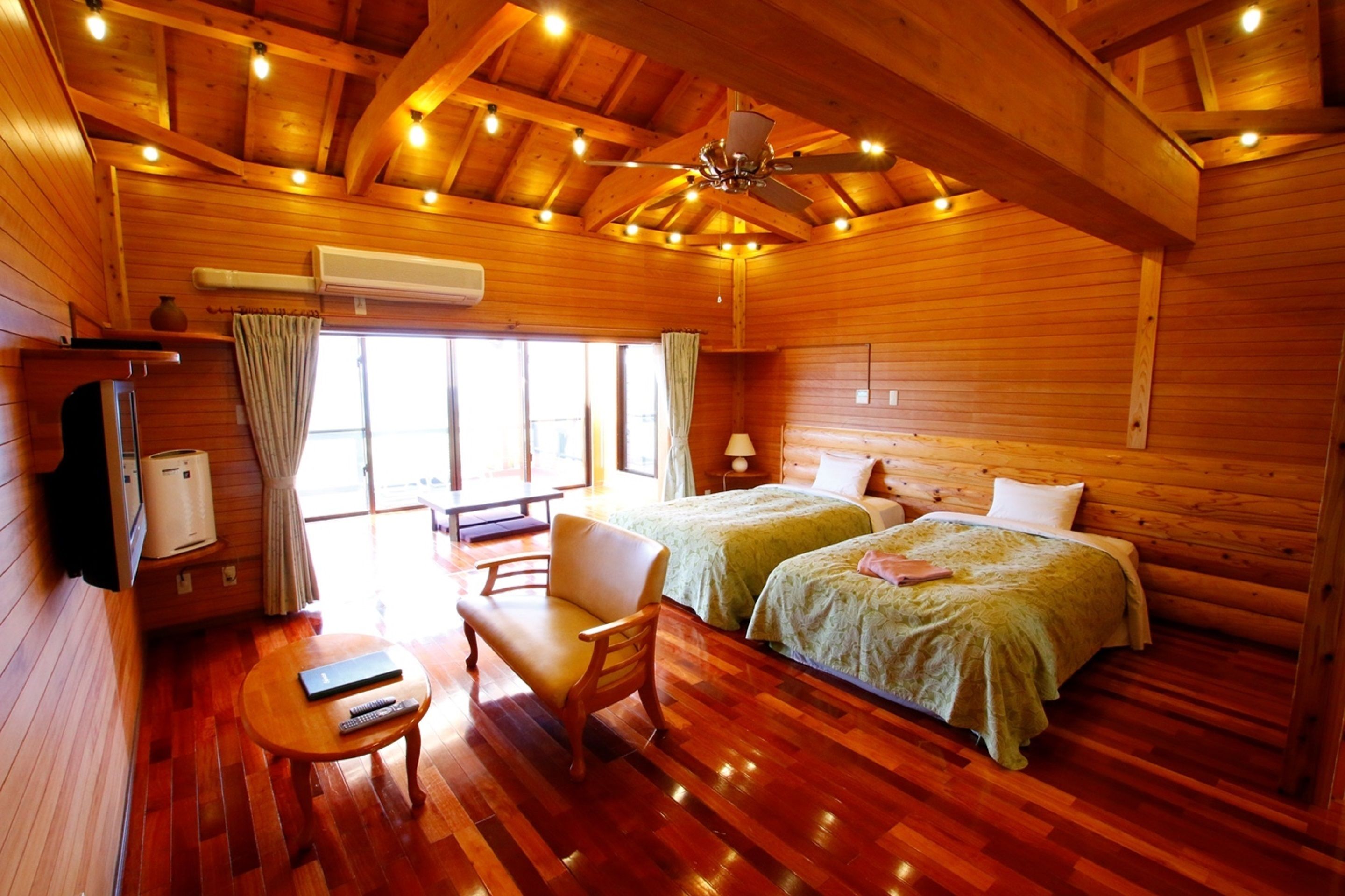 A wooden cabin with two beds, a sofa, a table, and a ceiling fan.