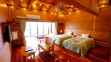A wooden cabin with two beds, a sofa, a table, and a ceiling fan.