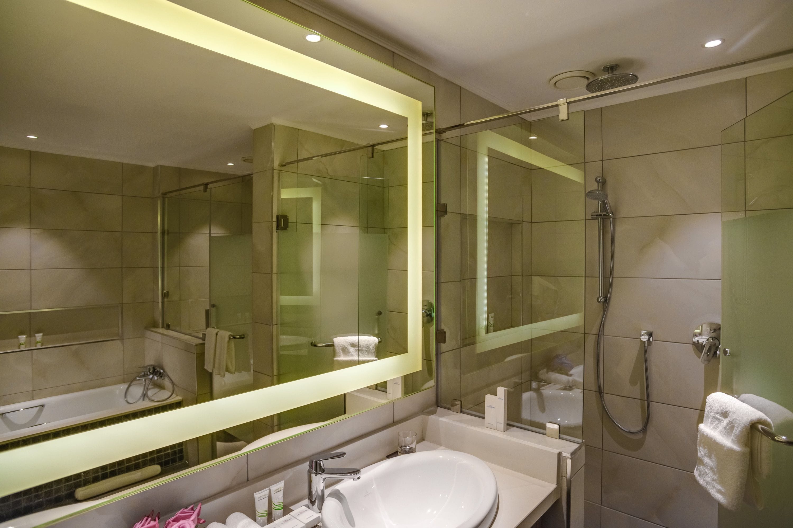 Une salle de bain moderne avec une douche à parois de verre, un grand miroir et un lavabo blanc.