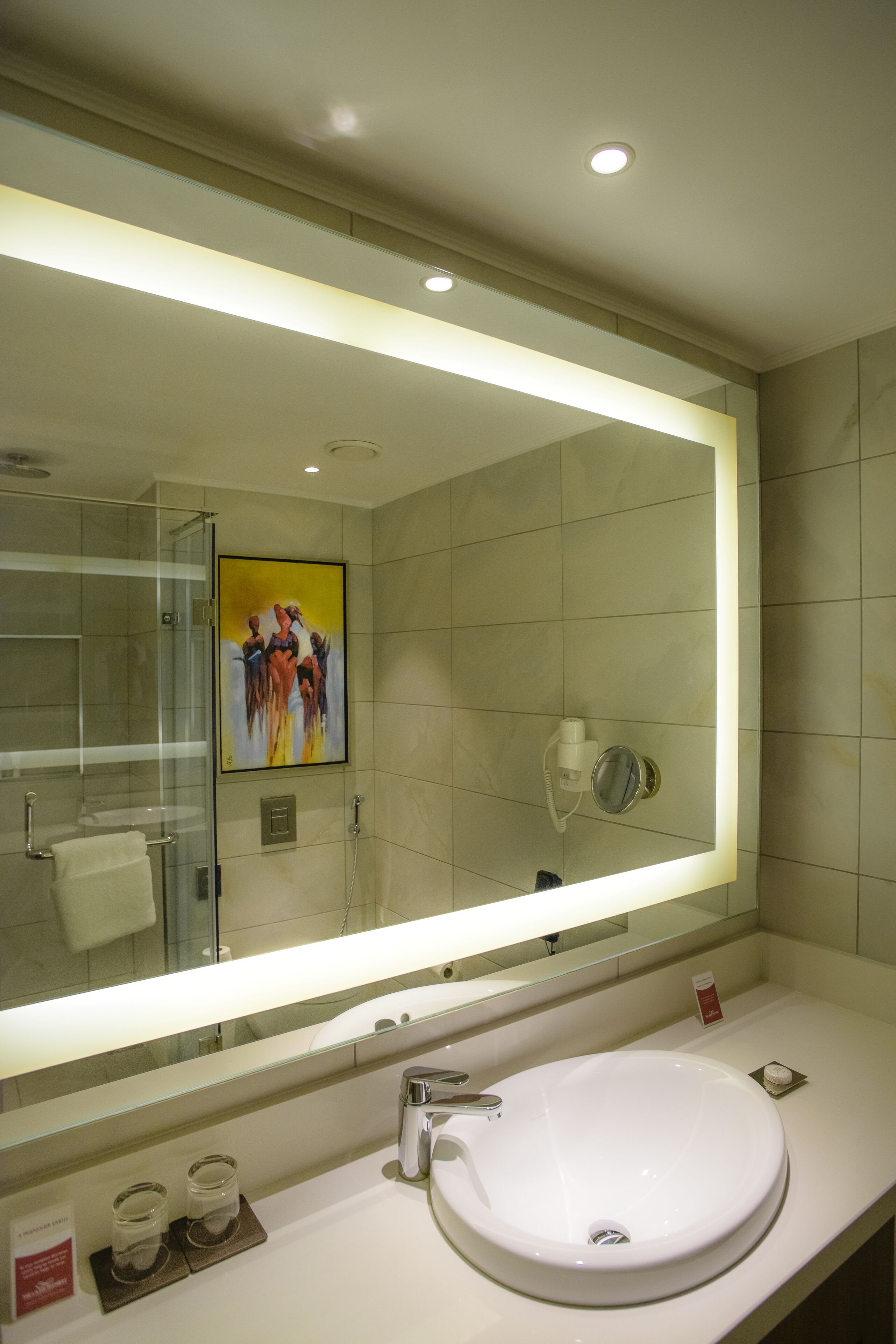 Ein Badezimmer mit einem großen Spiegel, einem weißen Waschbecken und einer Duschkabine aus Glas.