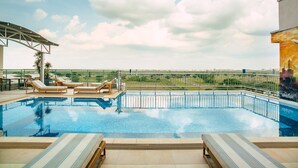 Una piscina infinita en la azotea con sillones de descanso, una pérgola y vistas al horizonte de la ciudad.