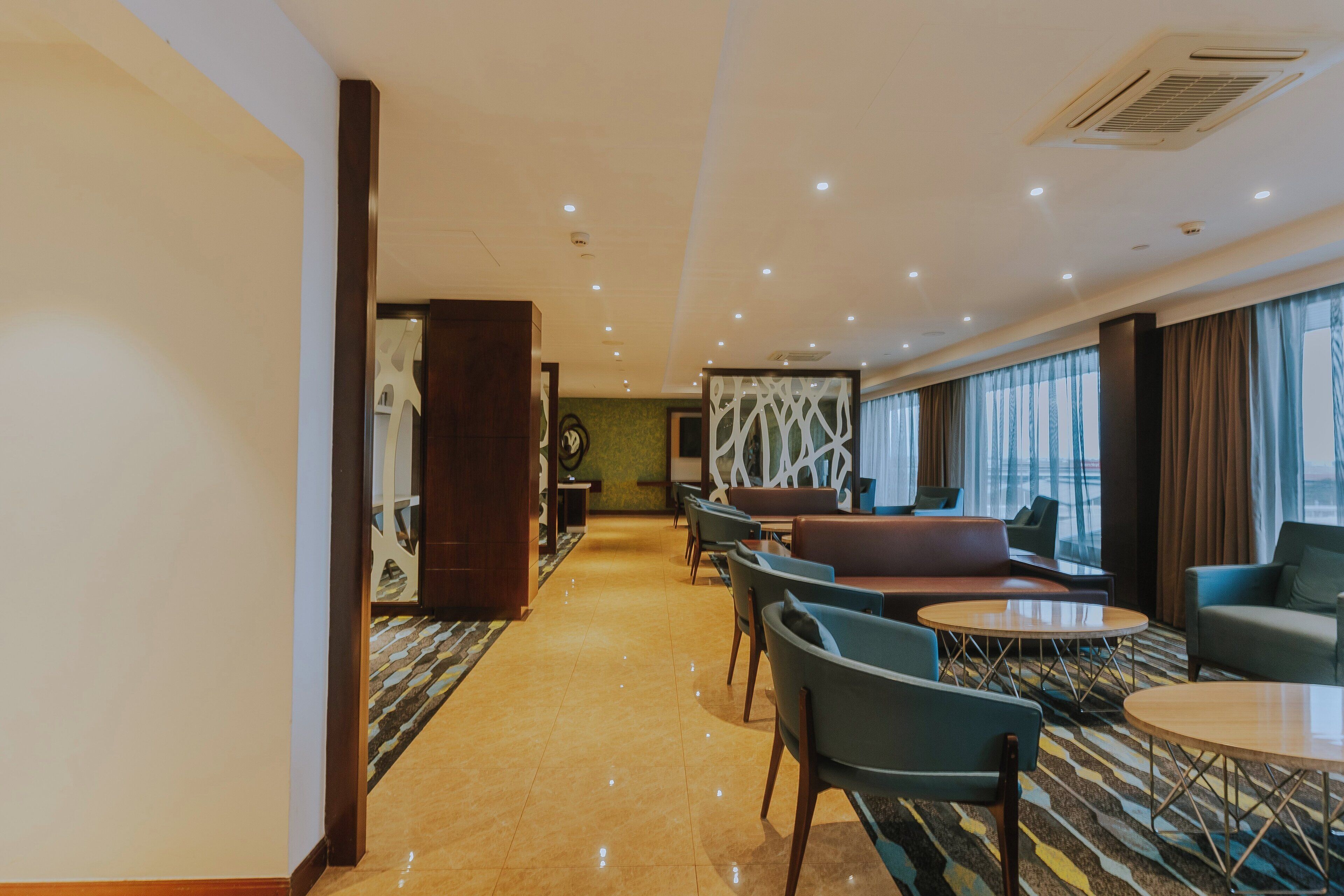 Un vestíbulo de hotel con una recepción, zona de estar y amplias ventanas con cortinas.