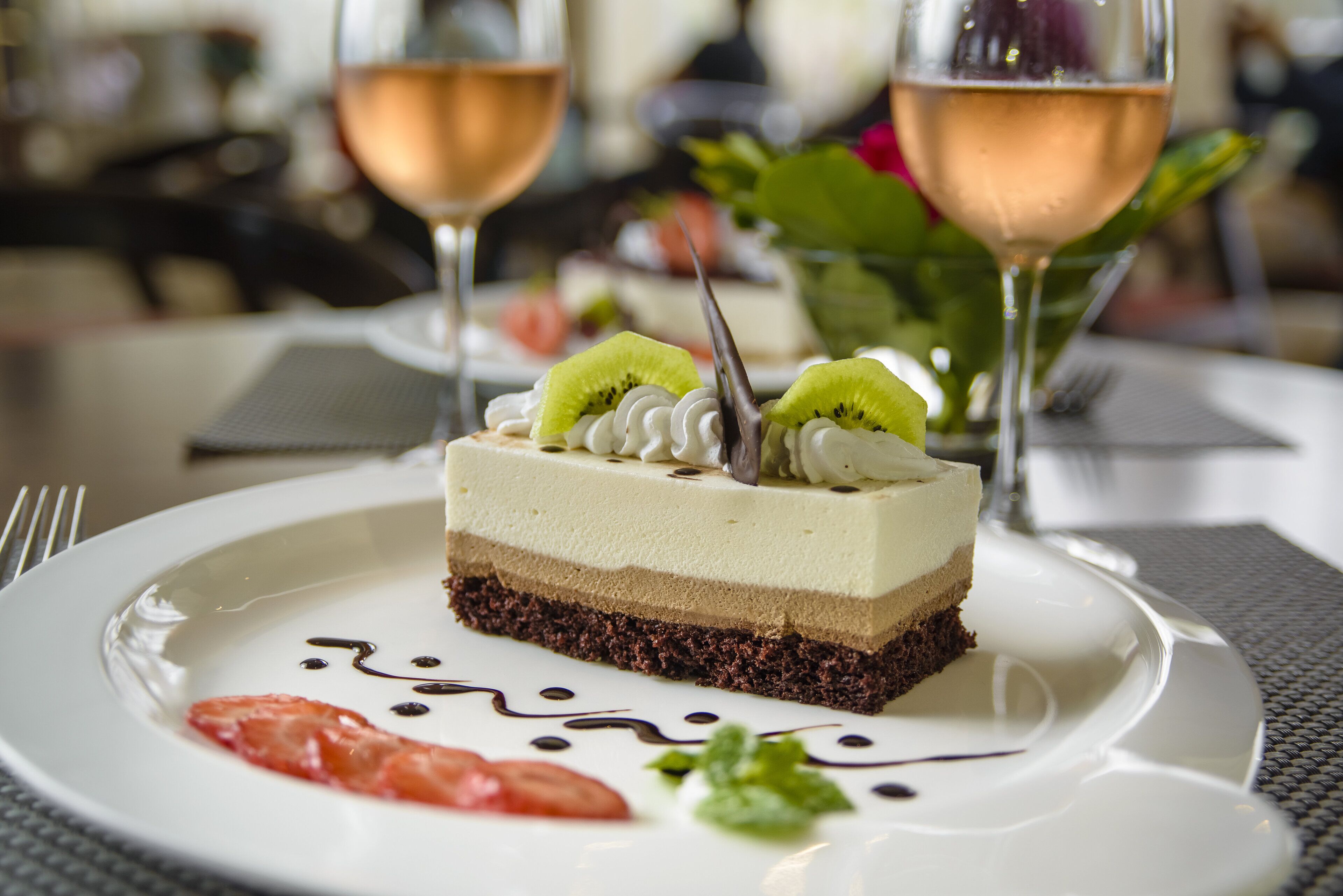 Una porción de postre en capas sobre un plato, acompañada de salsa y decoración, junto a dos vasos de una bebida de color claro.