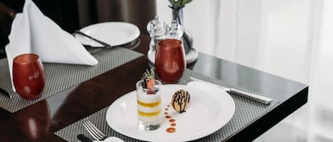 A table set for a meal with a dessert, a vase with red roses, and a clear glass.