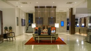 A spacious lobby with a curved glass railing, a reception desk, a seating area with a red rug, and a staircase leading to an upper level. - Crowne Plaza Nairobi Airport by IHG (Nairobi)