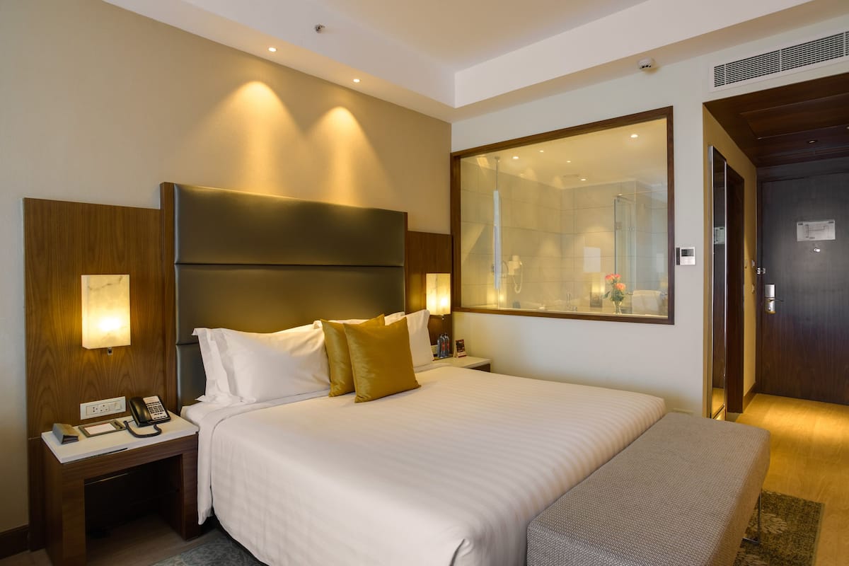 A hotel room with a large bed, bedside lamps, a nightstand with a phone, and a mirror above the bed.