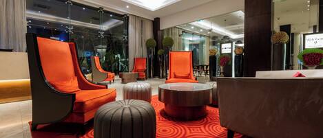 Un vestíbulo moderno con asientos naranja, una mesa de centro redonda y una alfombra con estampado rojo.