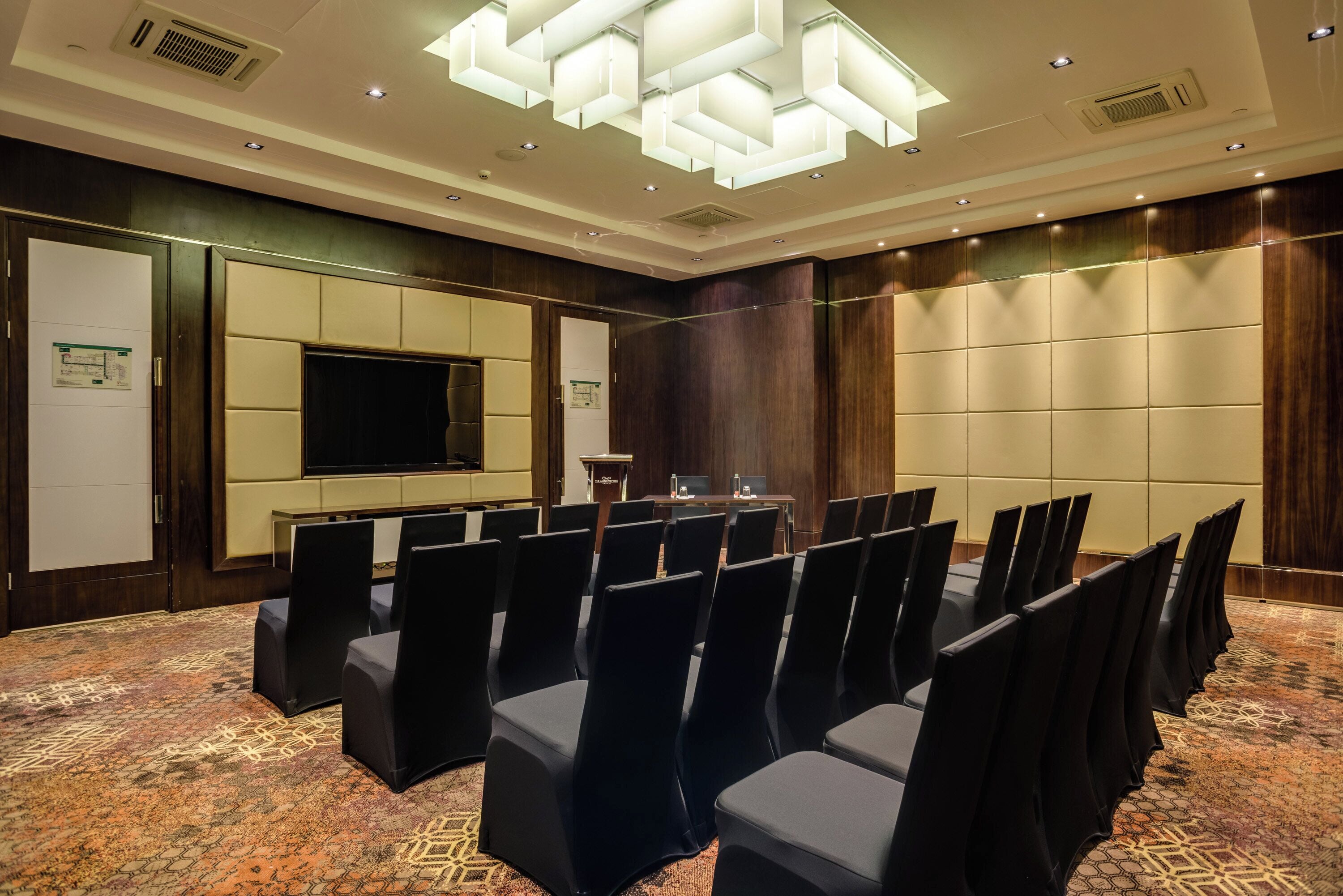 A conference room with rows of chairs, a large flat-screen TV, and a podium.