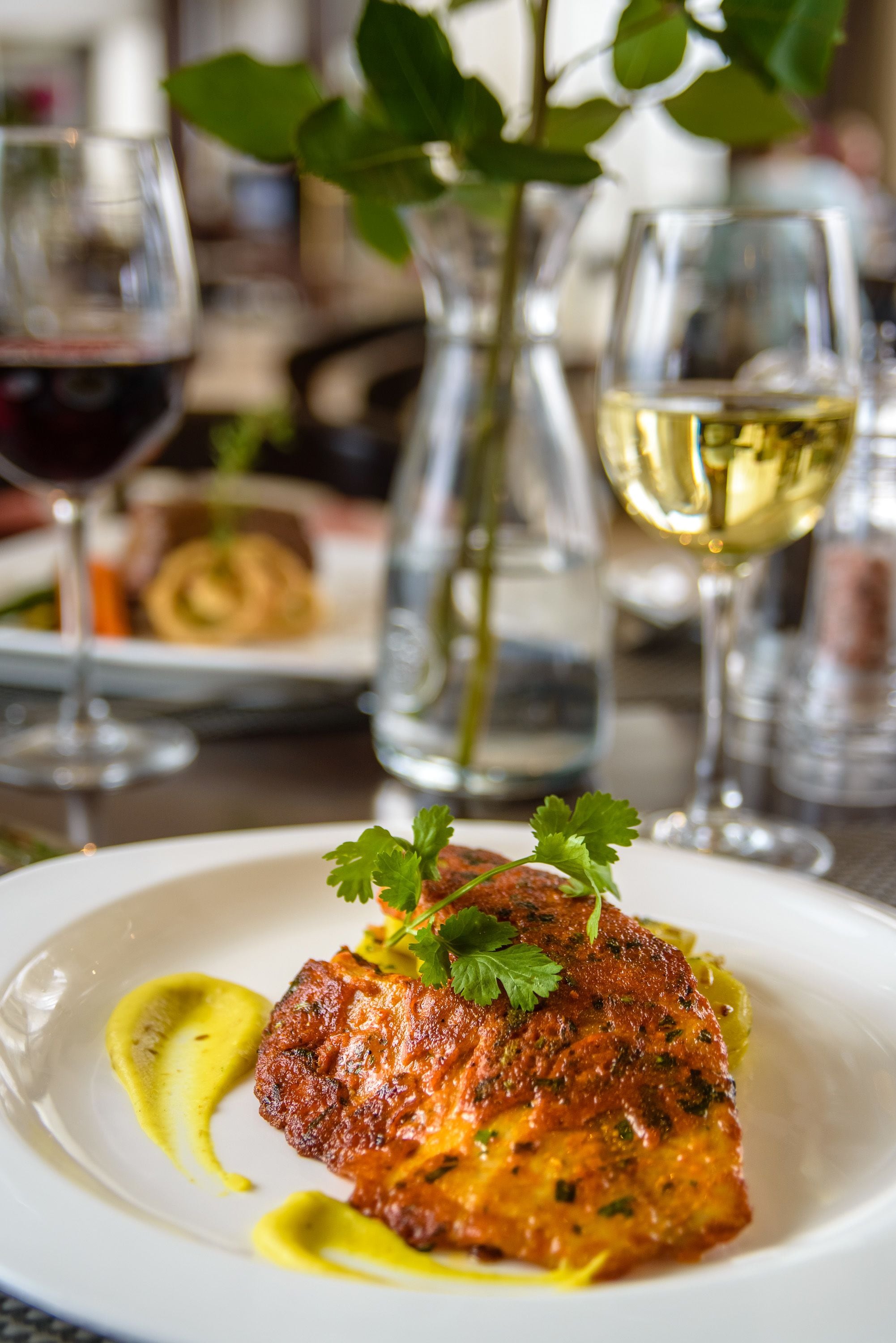 A plate of food with a garnish, a glass of red wine, and a glass of white wine on a table.