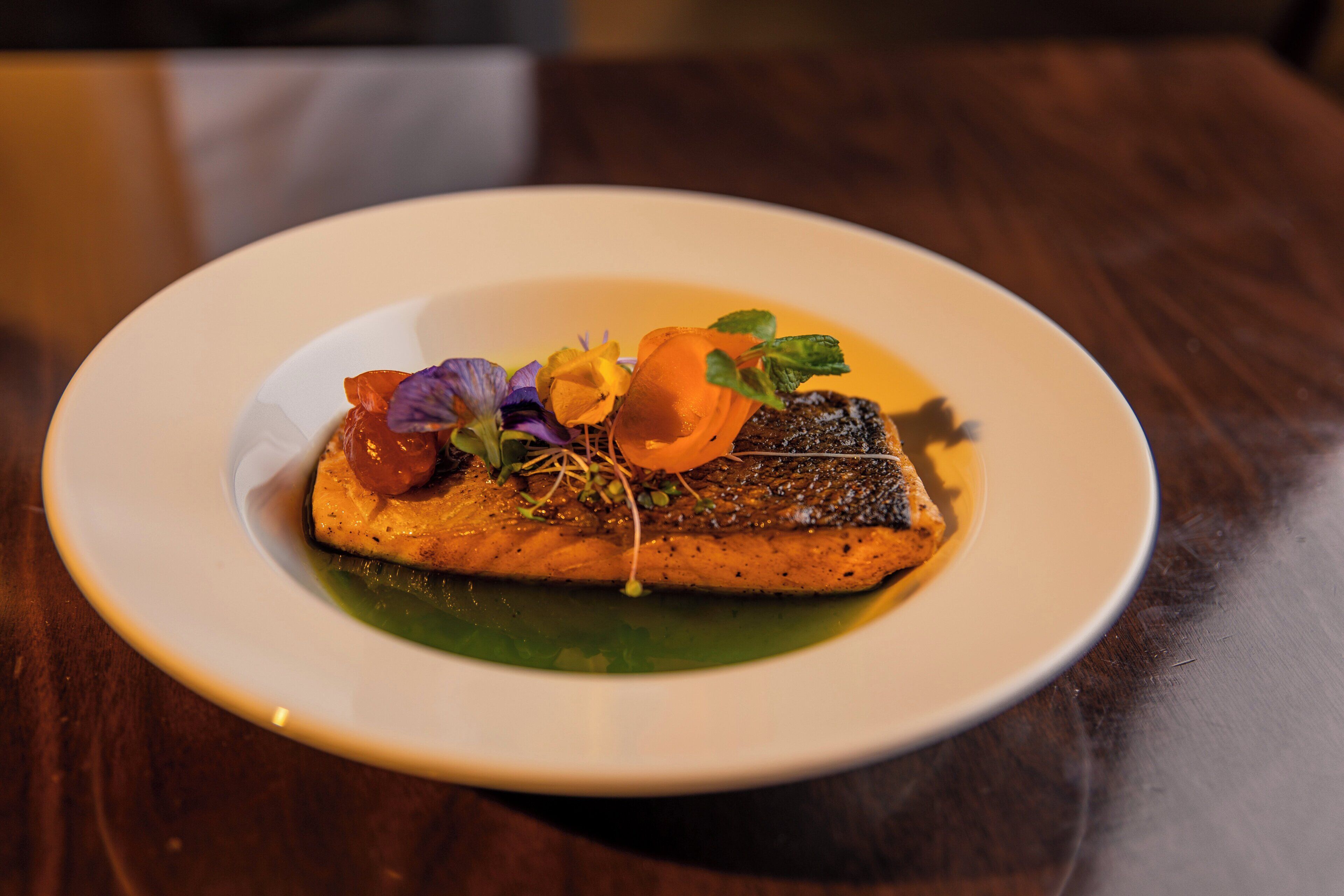 A plate with a piece of fish, garnished with herbs and edible flowers.