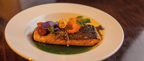 Un plato con un trozo de pescado, adornado con hierbas y flores comestibles.