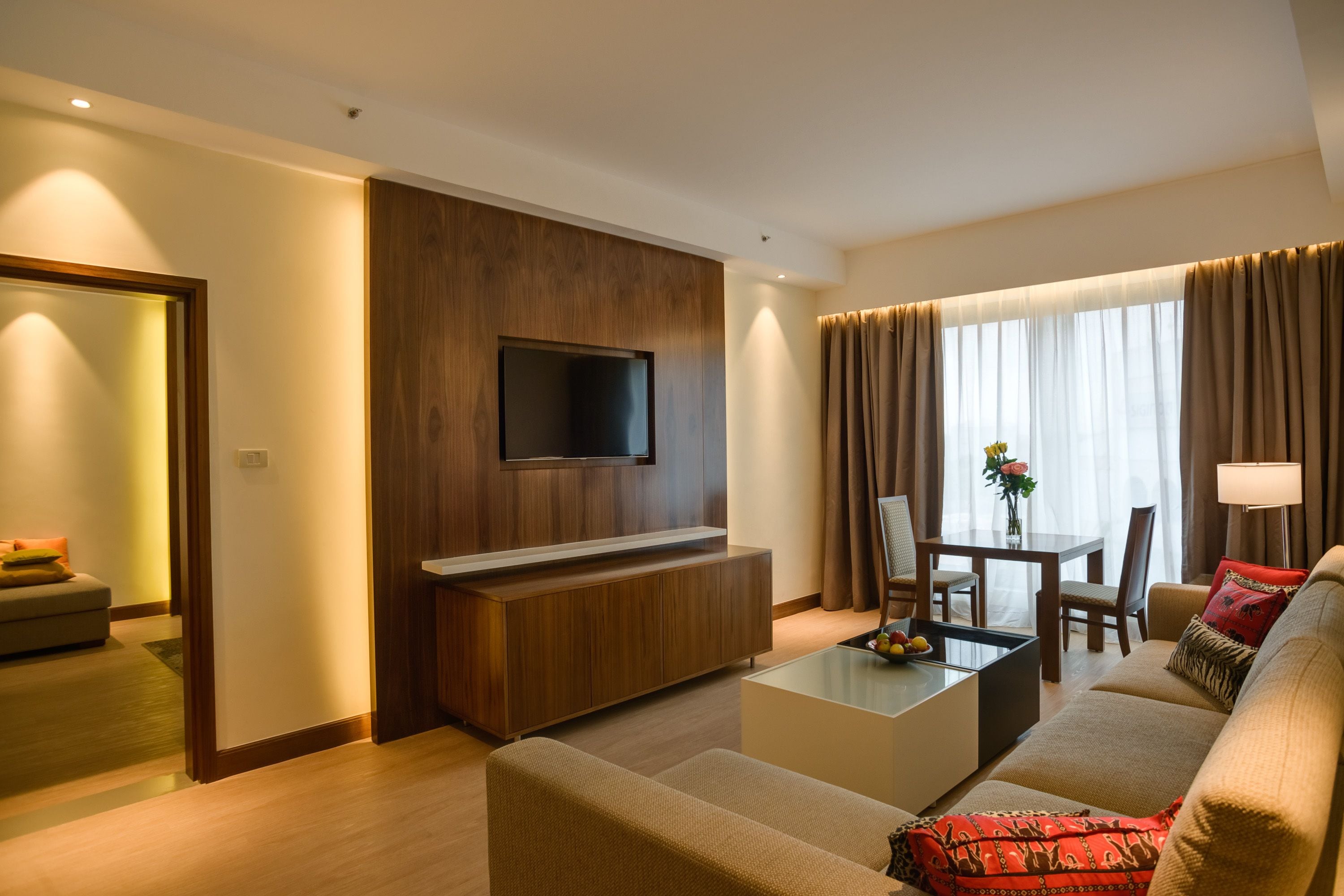 A modern living room with a flat-screen TV, a sofa, a coffee table, and a dining area with a table and chairs.