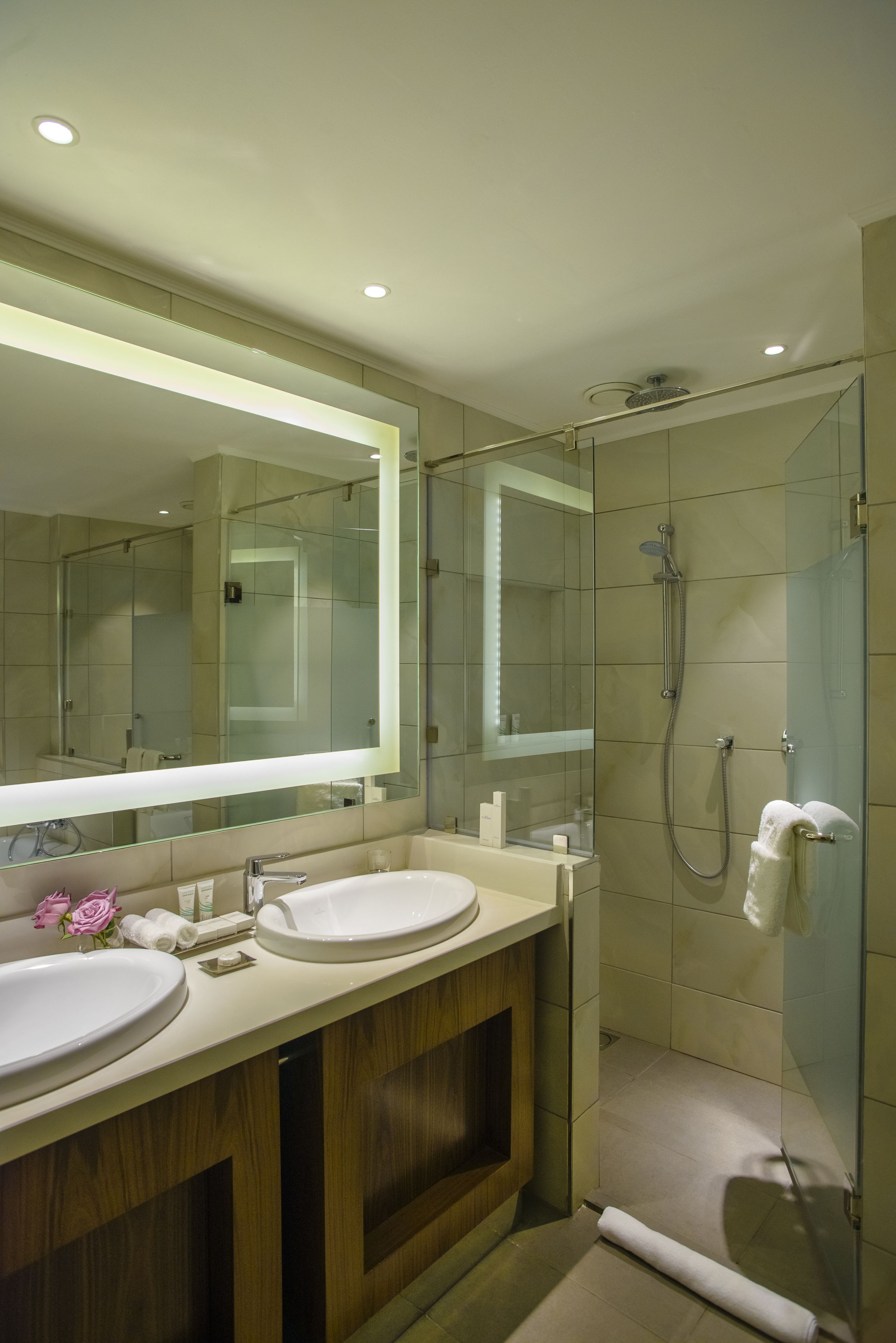 A modern bathroom with two sinks, a large mirror, and a glass-enclosed shower.