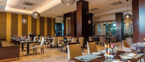 A spacious dining area with multiple tables and chairs, large pendant lights, and a modern interior design.