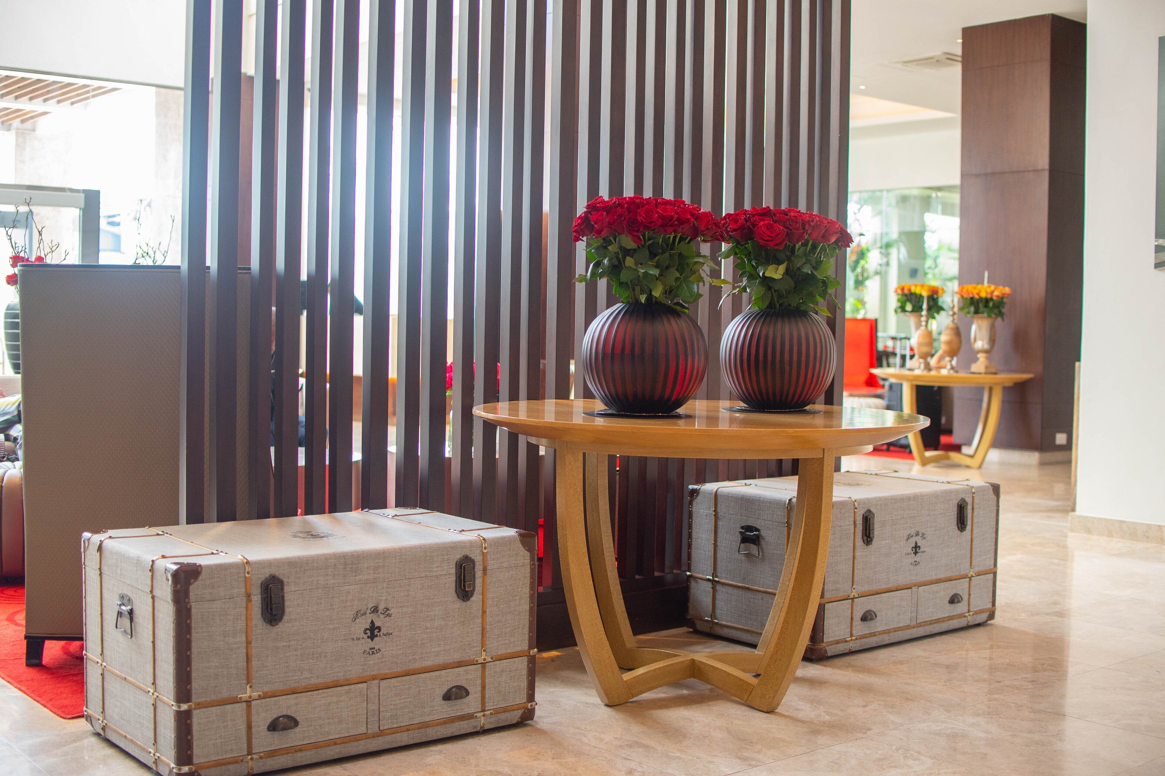 A room with a wooden table, two vases with red flowers, and vintage-style suitcases.