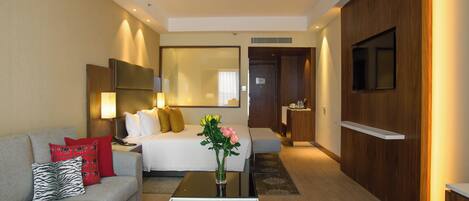 Una habitación de hotel con una cama, un sofá, una mesa de centro con fruta, un televisor y un espejo.