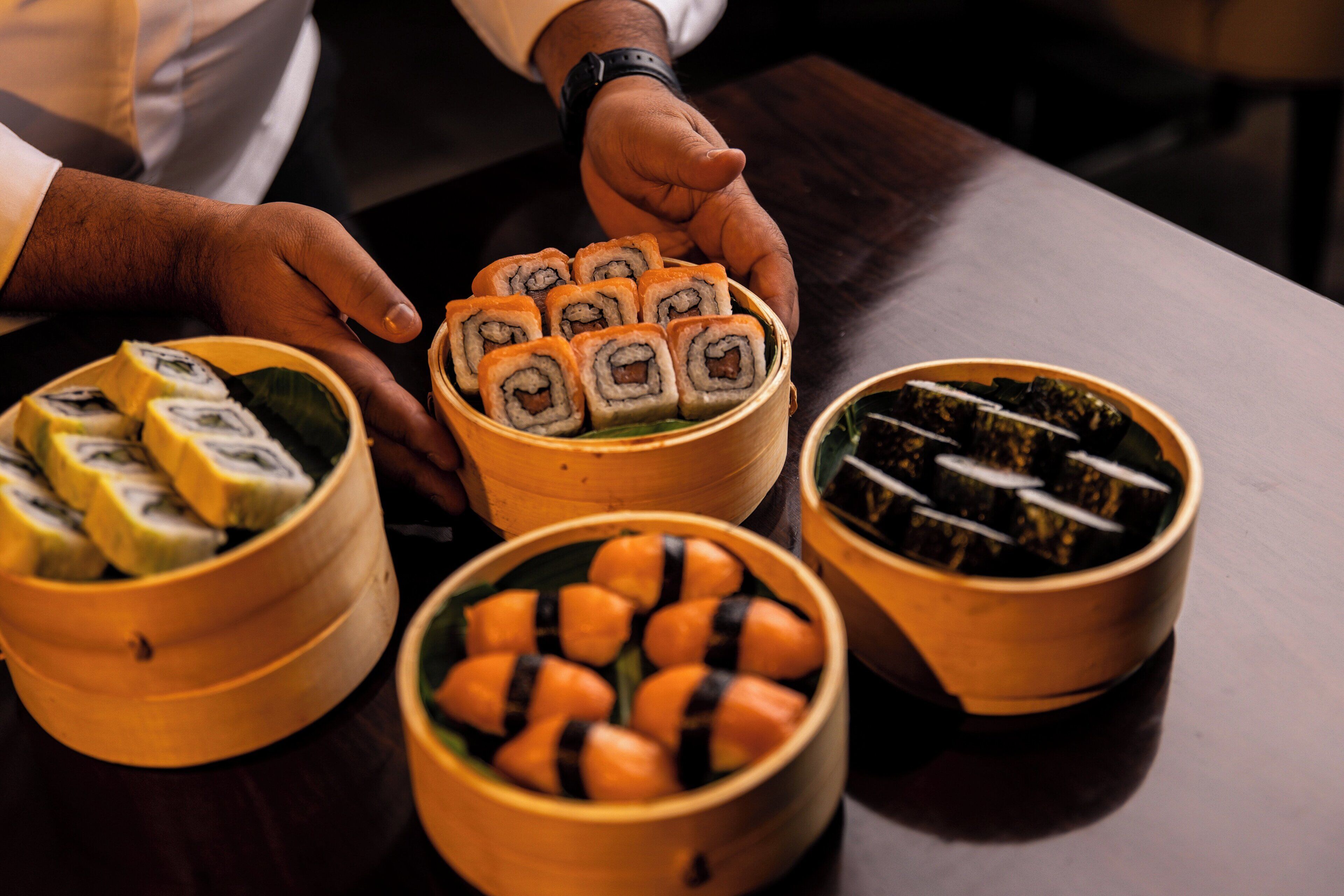 A table with three bamboo containers holding sushi rolls.