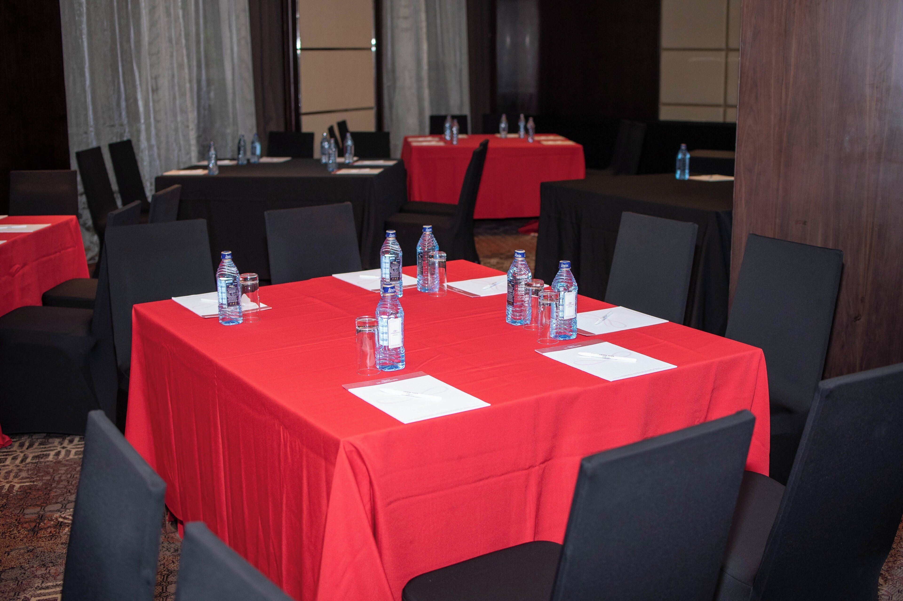A conference room with tables covered in red tablecloths, equipped with water bottles and glasses.