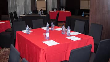 A conference room with tables covered in red tablecloths, equipped with water bottles and glasses.