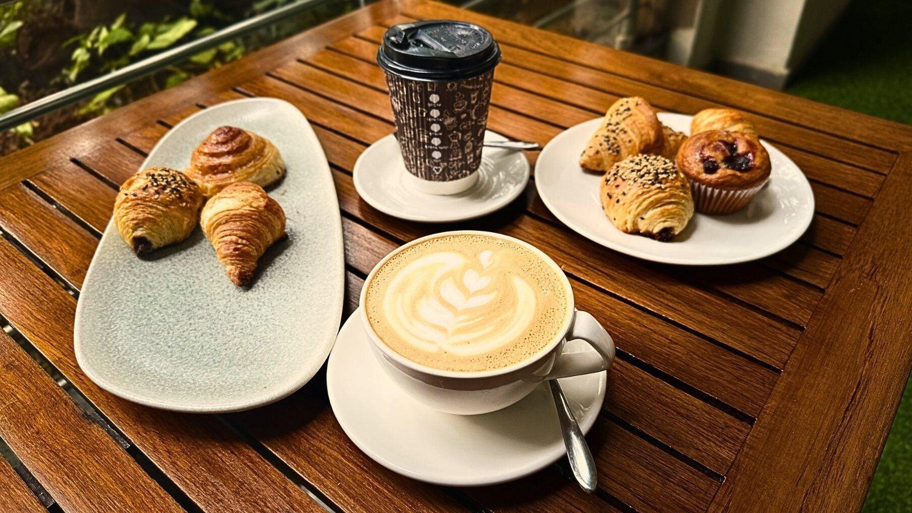 A table with a coffee cup, latte art, croissants, and pastries.