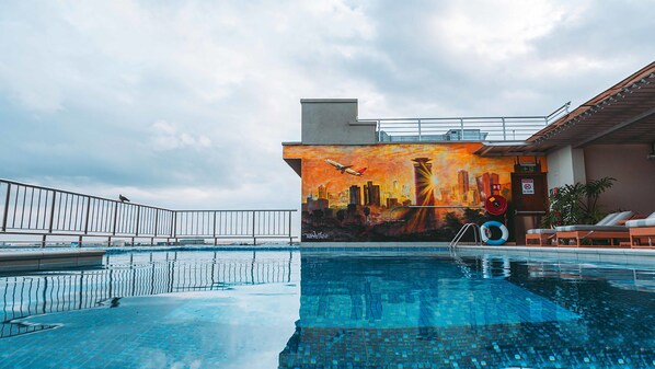 Una piscina en la azotea con un mural del paisaje urbano, sillas de descanso y barandilla.