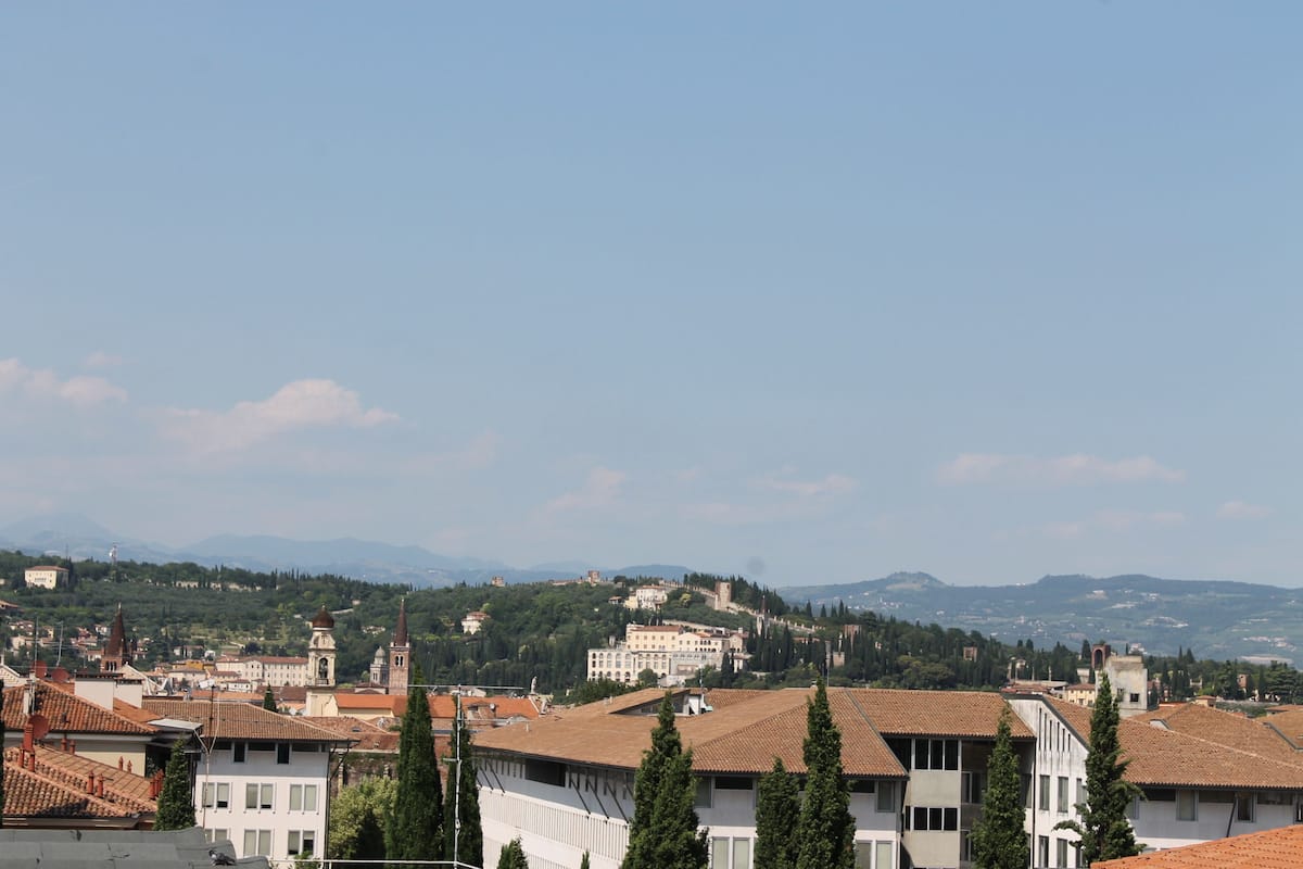 A cityscape with buildings, trees, and distant mountains under a clear sky.
