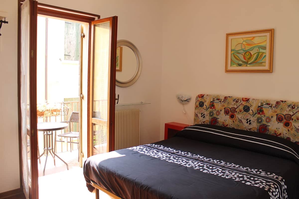 A bedroom with a bed, a bedside table, a mirror, and a window.