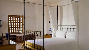 Un letto a baldacchino con tenda, una finestra in legno con decorazioni a griglia e un comodino con una lampada.