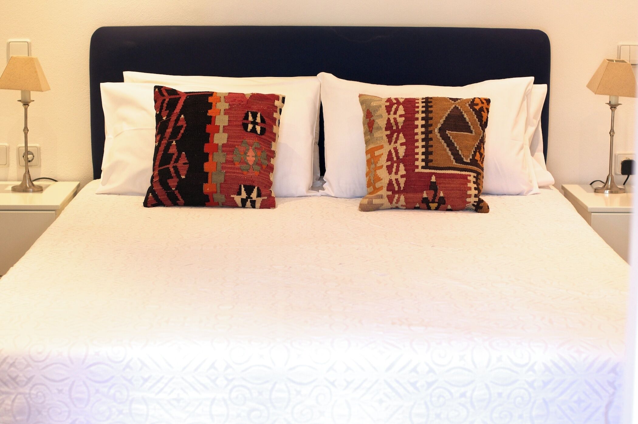 A bed with two patterned pillows, a dark headboard, and two bedside lamps.