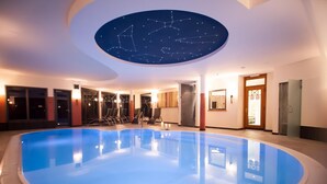 Ein großes Hallenbad mit Sternenhimmel-Design, umgeben von Liegestühlen und einem Holzboden.