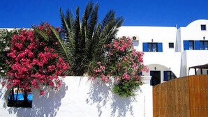A white building with blue shutters and pink flowers. - Santorini Breeze (Santorini)