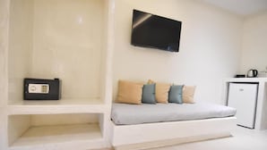 A modern room with a white sofa, a flat-screen TV mounted on the wall, and a small kitchenette area with a refrigerator and a kettle. - Santorini Breeze (Santorini)