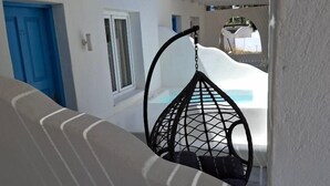 A white building with a blue door, a hanging chair, and a view of a blue sky. - Santorini Breeze (Santorini)