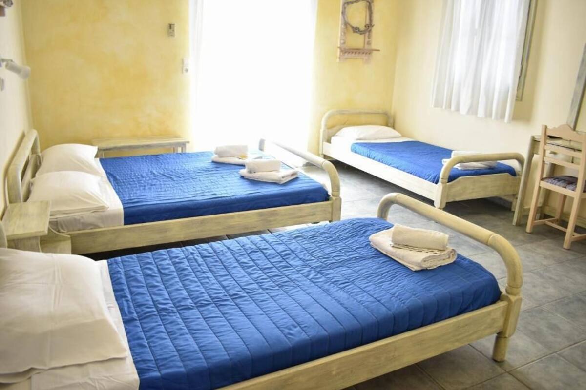 A room with three single beds, each with a blue quilt and white pillows.