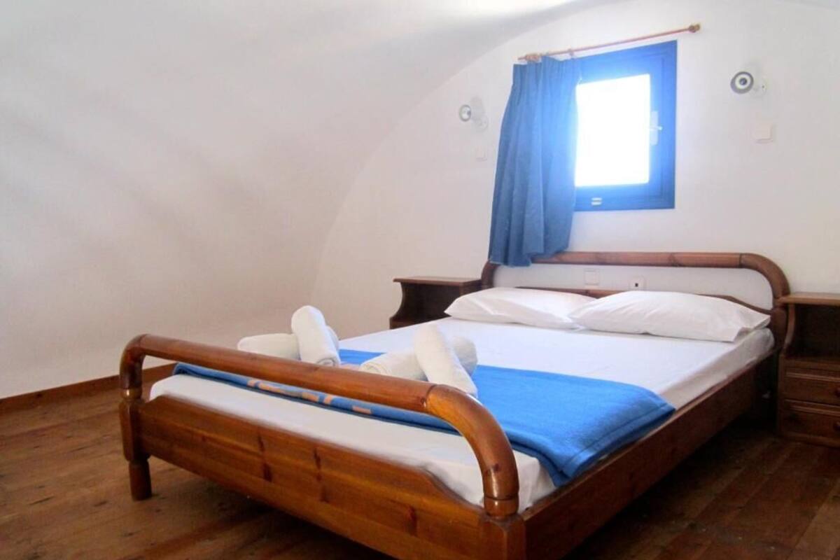 A single bedroom with a wooden bed, a small bedside table, and a window with a curtain.