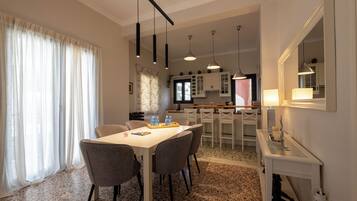 A dining area with a table and chairs, a kitchen in the background, and a mirror on the wall.