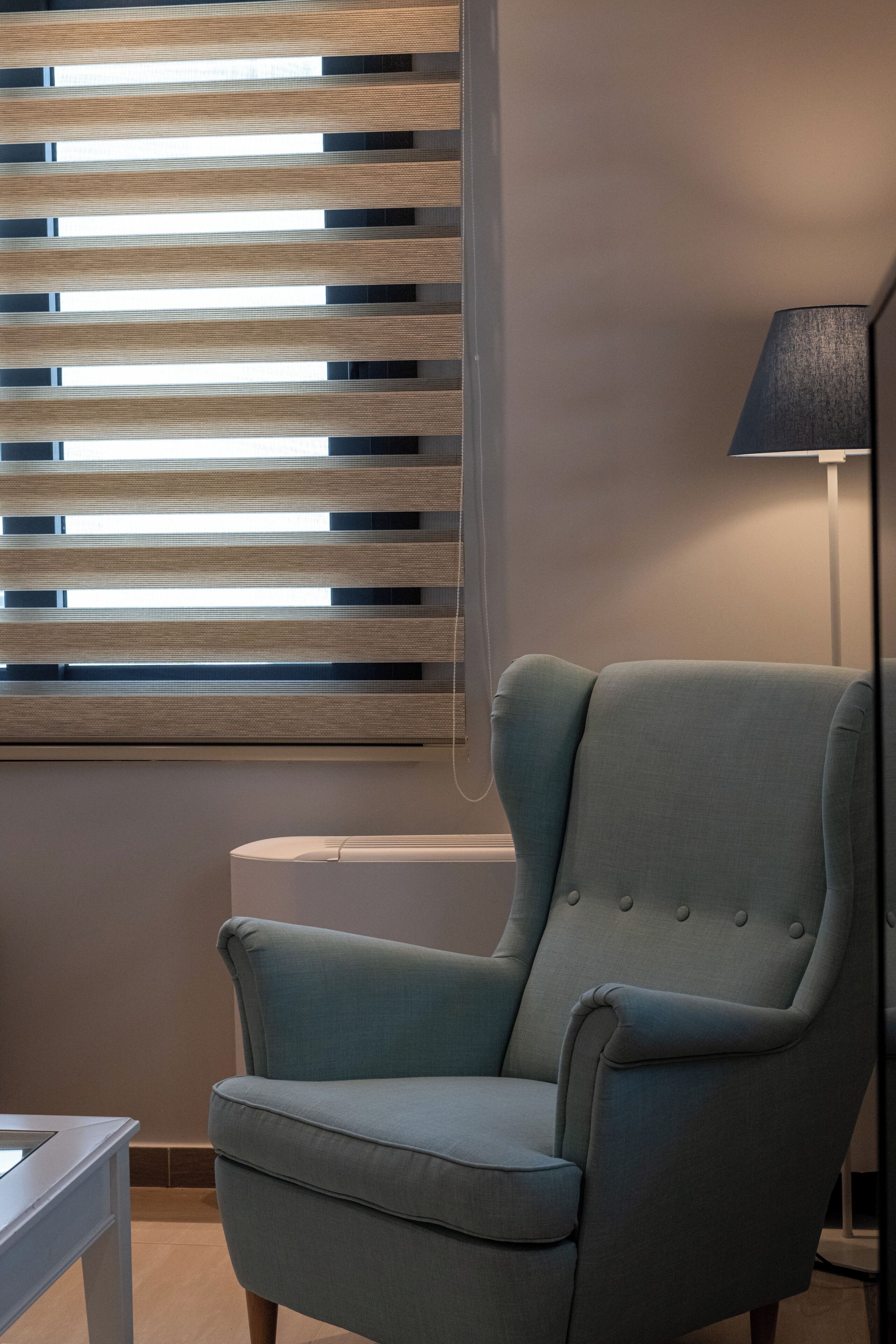A room with a light blue armchair, a floor lamp, and horizontal blinds.