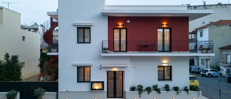 A modern two-story building with a balcony, a door, and potted plants.