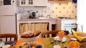 A kitchen with white cabinets, a microwave, a coffee maker, and a sink. There is a table with a basket of bread, a cup of coffee, and a plate of pastries. - Tata B&B (Rome)