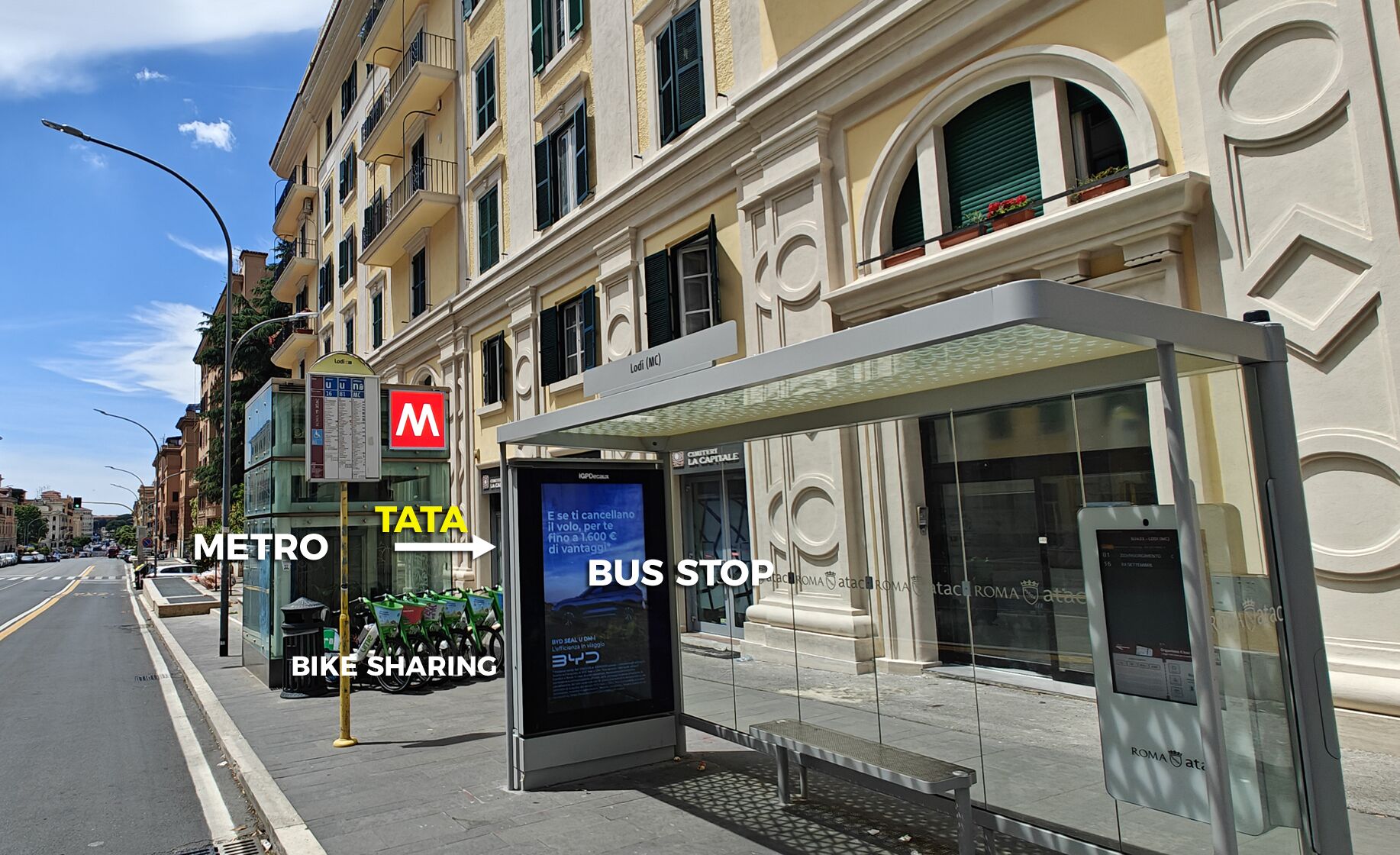 A bus stop with a shelter, a sign for the metro, and a bike-sharing station.