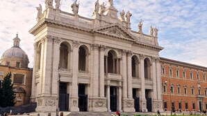 A large, classical building with multiple arches and statues on top. - Tata B&B (Rome)