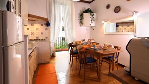 A kitchen with a dining area, wooden cabinets, a refrigerator, and a window with curtains. - Tata B&B (Rome)